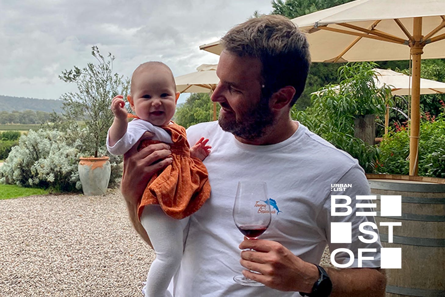 A person standing at a kid-friendly restaurant Melbourne with a baby and a glass of wine.